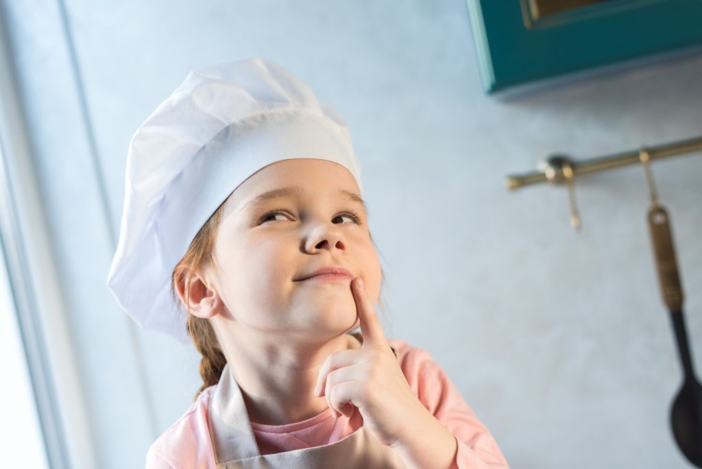 adorable child in chef hat smiling and looking away in kitchen